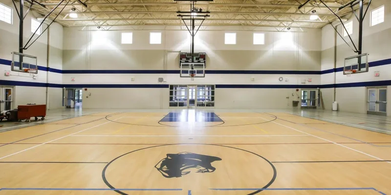 Bright and spacious gymnasium with polished hardwood floors, multiple basketball hoops, and ample natural light, ideal for recreation.