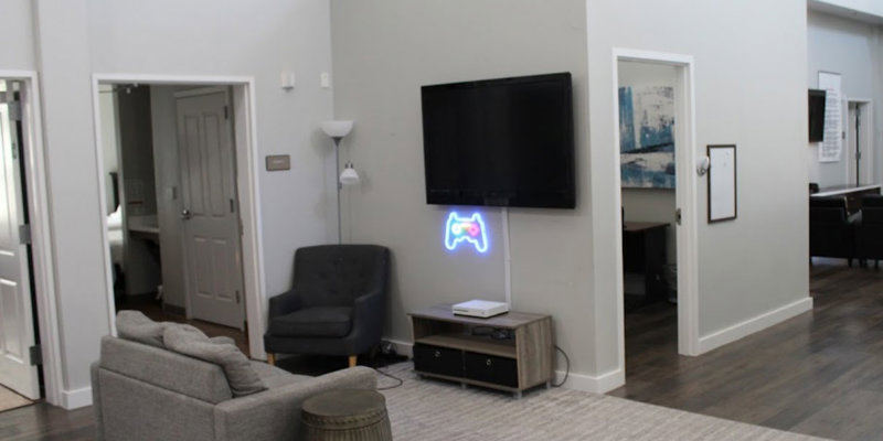  A cozy entertainment area featuring a TV, comfortable seating, and a neon game controller sign, creating a fun and relaxed atmosphere for leisure.