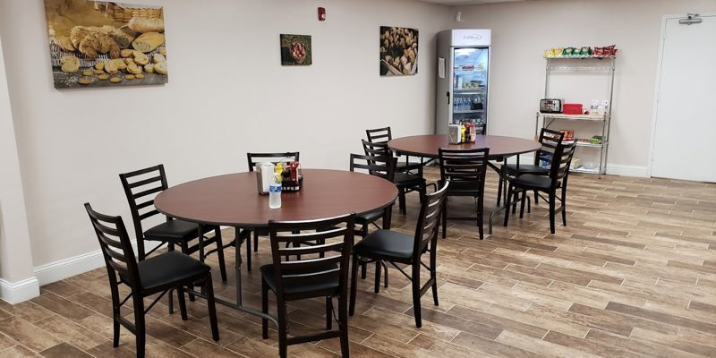 A cozy dining area with round tables, chairs, a stocked fridge, and snack shelves, creating a welcoming space for meals and relaxation.