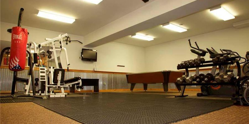 A well-equipped gym room featuring a variety of exercise machines, weights, a punching bag, and a pool table, perfect for staying active.