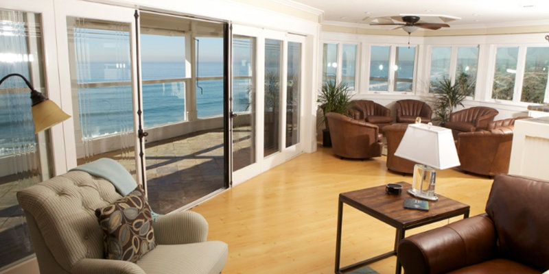 A bright lounge area with ocean views features cozy seating, warm wood floors, and large windows that bring in plenty of natural light.