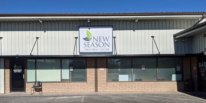 The exterior of a welcoming treatment center, featuring a large "New Season" sign, a simple design, and a bright, sunny atmosphere.