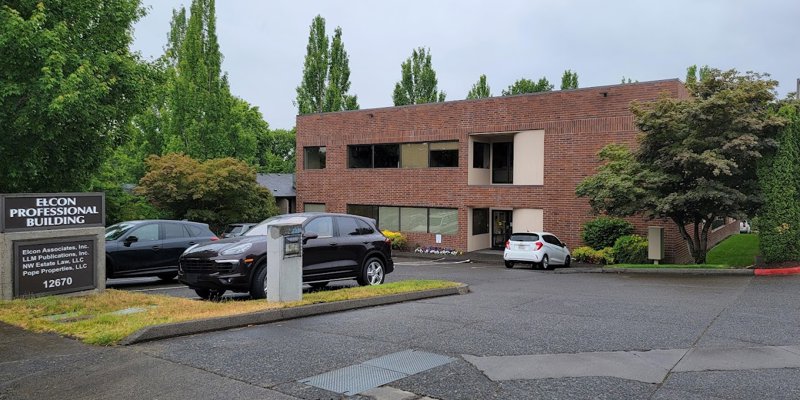  A professional two-story brick building surrounded by lush greenery and parked cars, creating a clean and inviting business environment.