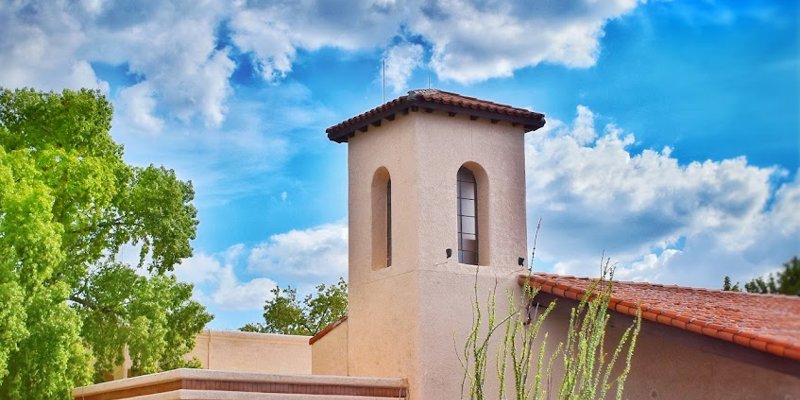  A bright, sunny day highlights a charming building with a Spanish-style tower, surrounded by desert landscaping and vibrant greenery.