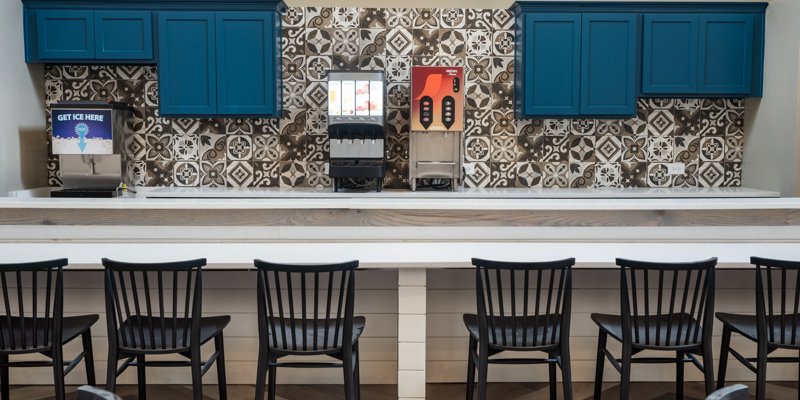 A stylish beverage station with patterned tile backsplash, blue cabinets, and a modern seating area, offering a comfortable place to relax.