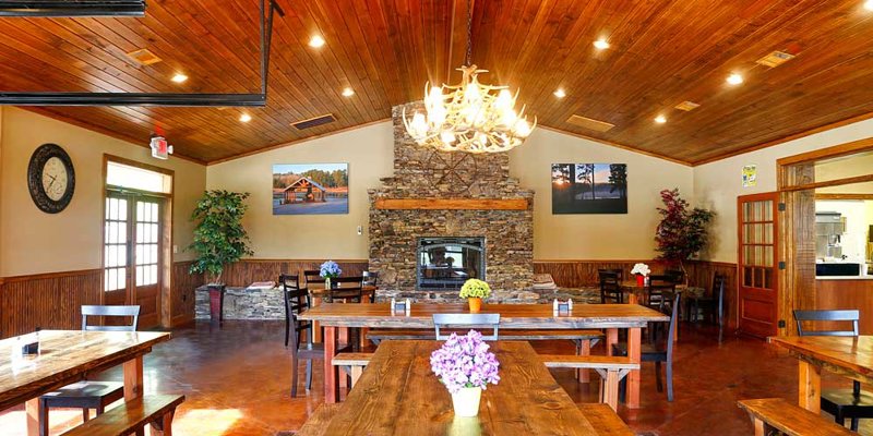 A cozy dining area with wooden tables, a stone fireplace, warm lighting, and a chandelier, creating an inviting and rustic atmosphere.