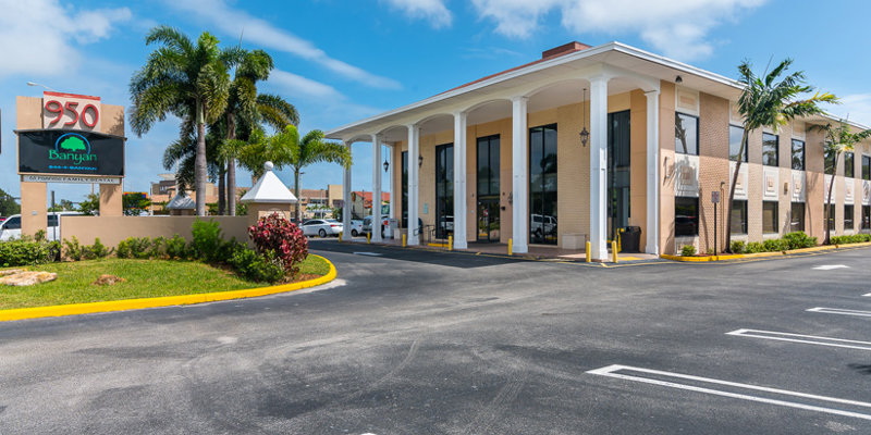  A bright and inviting building with tall columns, large windows, and a well-maintained parking lot. The surrounding palm trees and clear skies create a tropical, welcoming atmosphere.