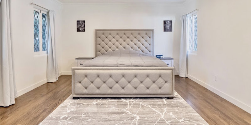 A spacious, well-lit bedroom featuring a luxurious upholstered bed, elegant hardwood floors, and a soft area rug for added comfort.