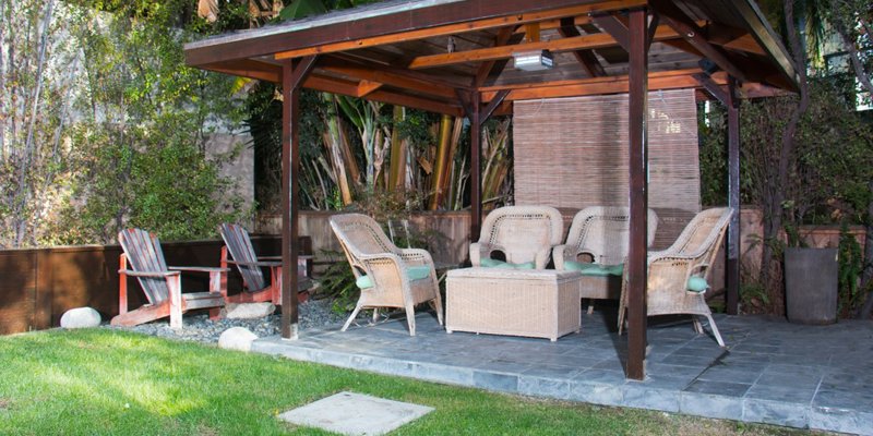 Charming garden gazebo with wicker seating and lush greenery, offering a cozy and shaded space perfect for relaxation and conversations.