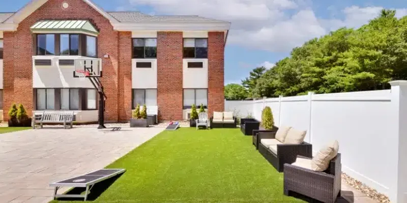 Outdoor recreation area with a basketball hoop, cornhole game, and cozy seating on a manicured lawn, ideal for relaxation and fun.