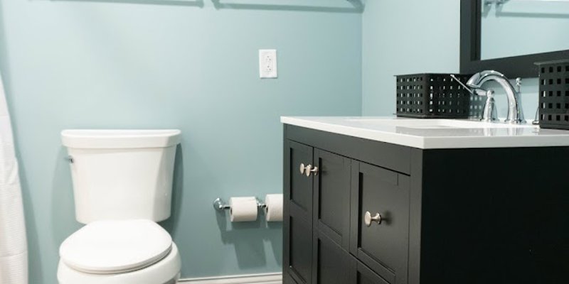 A modern, clean bathroom with a black vanity, white fixtures, and light blue walls, offering a fresh and inviting space for comfort.