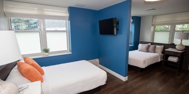 Cozy double bedroom with modern decor, featuring bright blue walls, warm lighting, and large windows that fill the space with natural light.