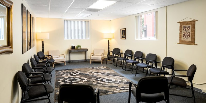  A bright and welcoming group room with chairs arranged in a circle, soft lighting, and warm decor. The patterned rug adds to the cozy atmosphere.