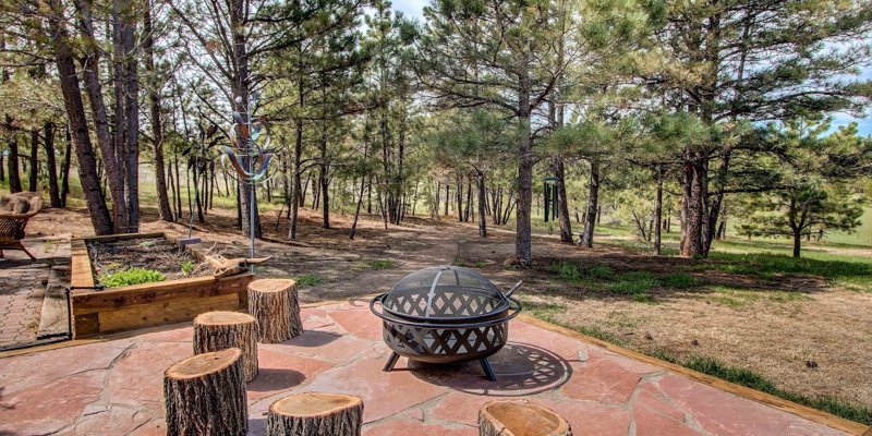  A peaceful outdoor fire pit area surrounded by tall trees, featuring rustic log stools and a charming flagstone patio, perfect for relaxation.